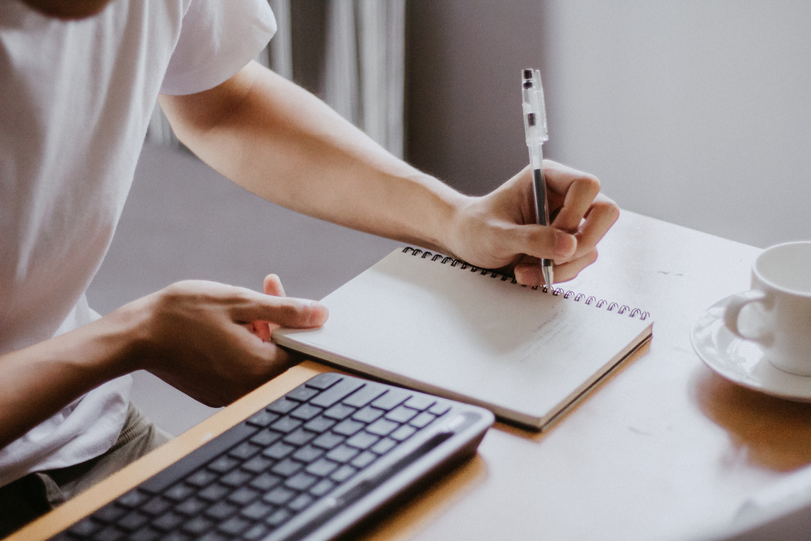 Student Writing on Notebook During Online Class